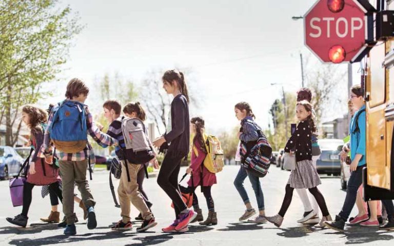 Young children exiting school bus and crossing street