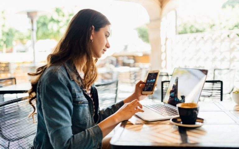 woman working on phone and laptop from coffeeshop