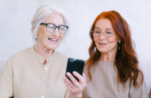 Two senior women call rideshare on phone.